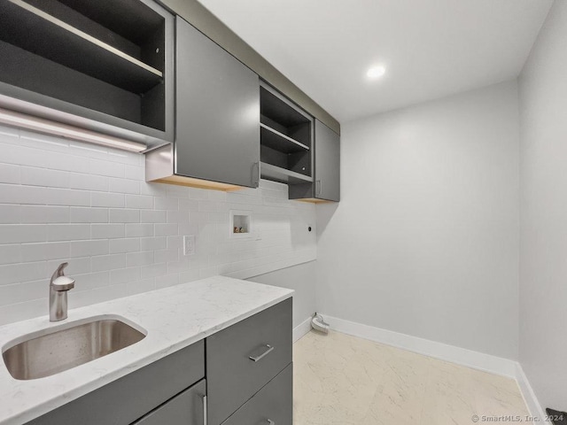 interior space featuring gray cabinets, tasteful backsplash, light stone counters, and sink