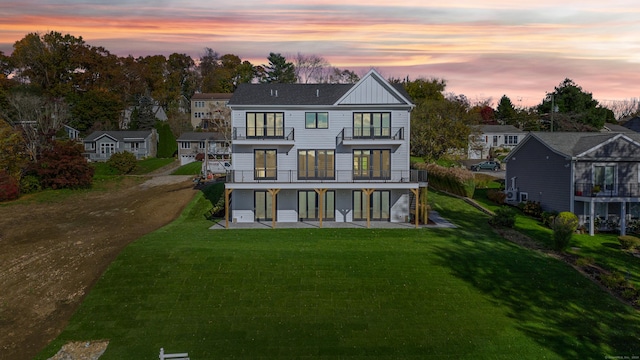 back house at dusk featuring a yard, a patio area, and a balcony