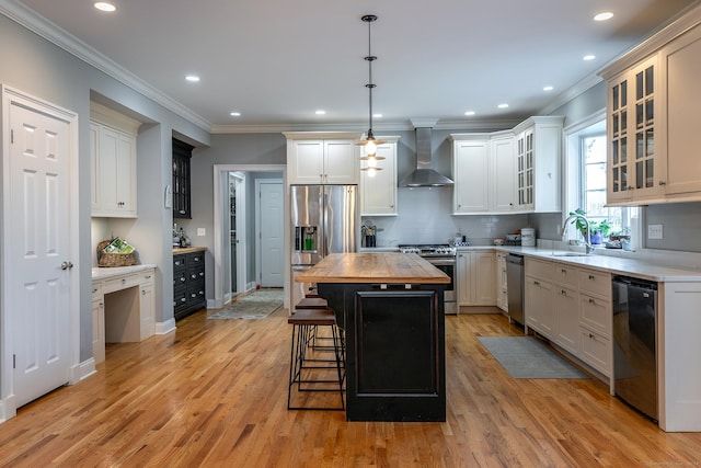 kitchen with wooden counters, appliances with stainless steel finishes, wall chimney range hood, light hardwood / wood-style flooring, and a kitchen island