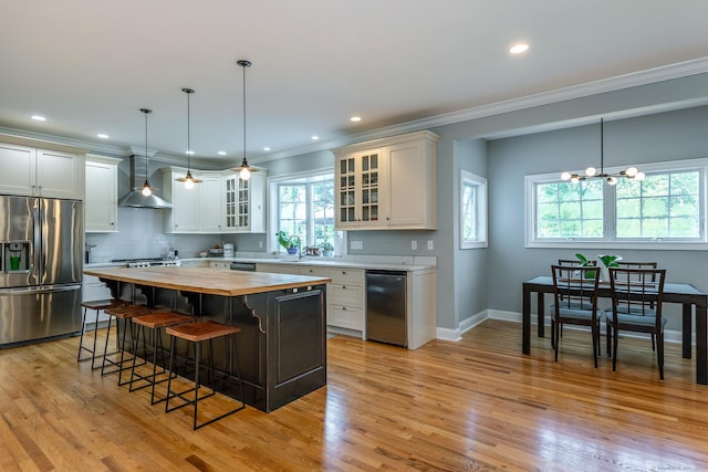 kitchen with wall chimney exhaust hood, a center island, stainless steel appliances, and a wealth of natural light