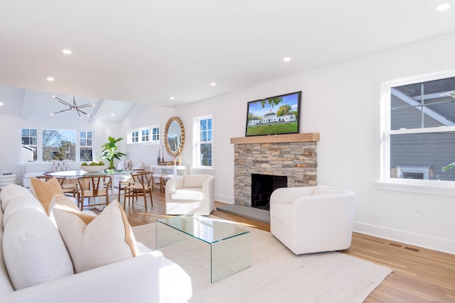 living room featuring a chandelier, a healthy amount of sunlight, a fireplace, and light hardwood / wood-style flooring