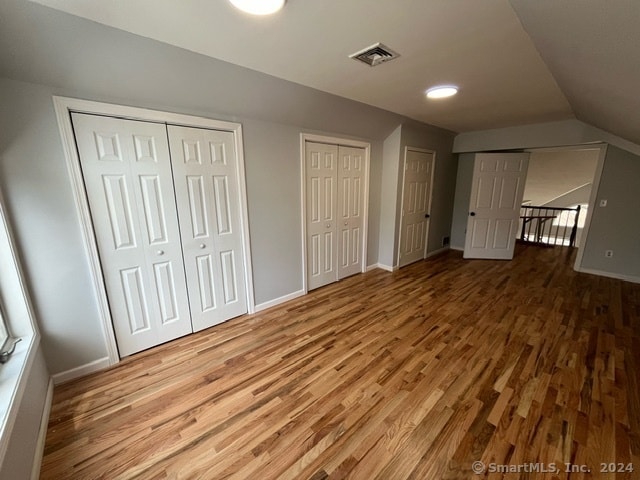 unfurnished bedroom featuring light hardwood / wood-style flooring, two closets, and lofted ceiling