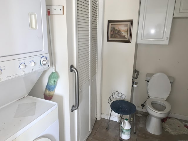 washroom featuring stacked washer and dryer and dark tile patterned flooring