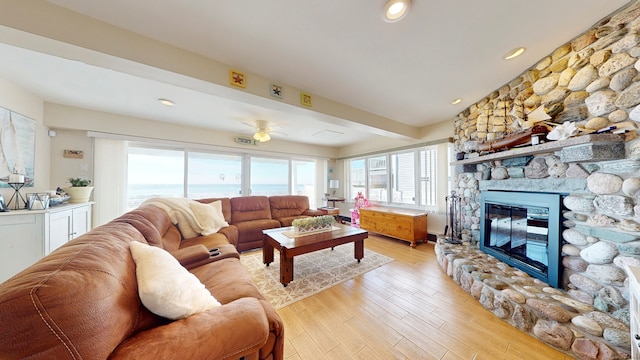 living room with ceiling fan, a stone fireplace, light hardwood / wood-style floors, and a water view