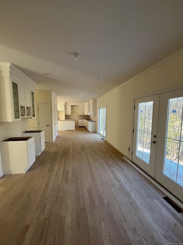 unfurnished living room featuring crown molding, french doors, and light hardwood / wood-style flooring