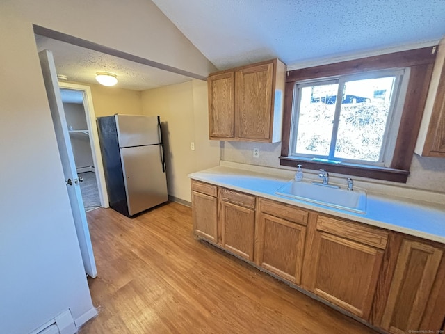 kitchen featuring sink, a textured ceiling, stainless steel refrigerator, a baseboard radiator, and light hardwood / wood-style floors