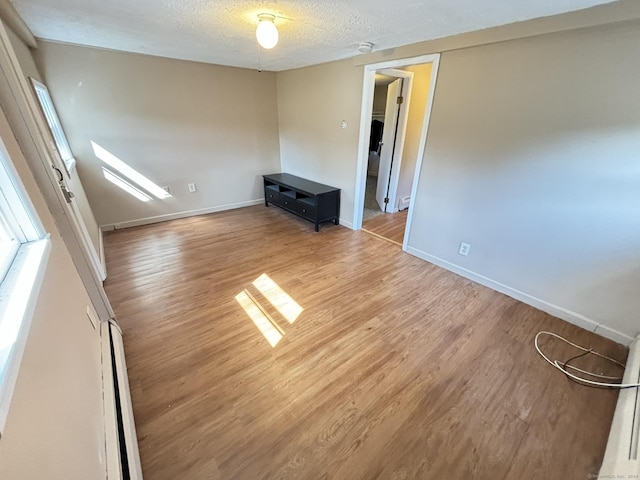 unfurnished living room with wood-type flooring, a textured ceiling, and baseboard heating