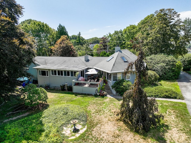 rear view of property with roof with shingles, a chimney, a yard, and a wooden deck