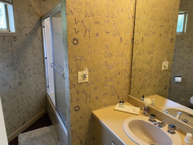 bathroom featuring combined bath / shower with glass door, a healthy amount of sunlight, vanity, and wallpapered walls