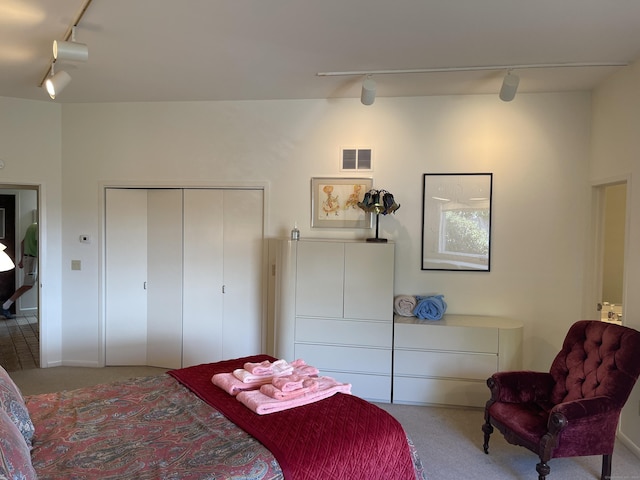 carpeted bedroom featuring track lighting, visible vents, and a closet