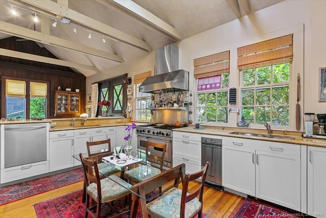 kitchen with sink, appliances with stainless steel finishes, light hardwood / wood-style flooring, lofted ceiling with beams, and wall chimney range hood