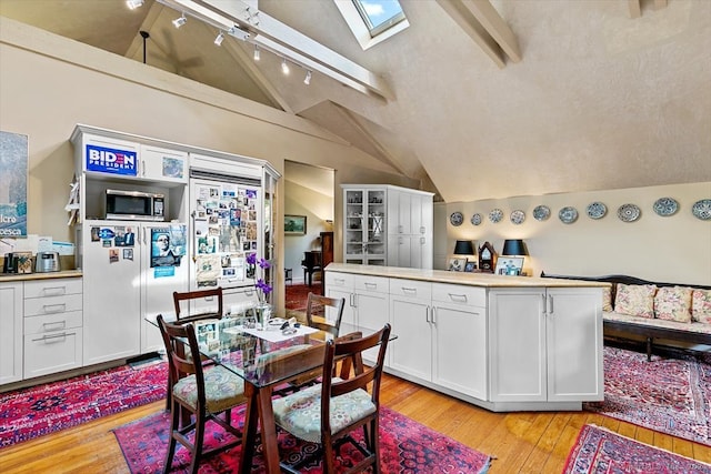 dining room featuring a skylight, light hardwood / wood-style flooring, high vaulted ceiling, and beamed ceiling