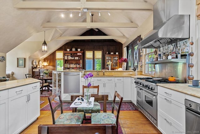 kitchen with stainless steel appliances, vaulted ceiling with beams, wall chimney exhaust hood, and white cabinetry