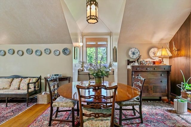 dining space featuring wooden walls, lofted ceiling, and wood-type flooring