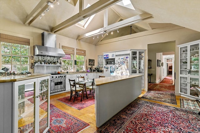 kitchen featuring a skylight, rail lighting, stainless steel range, high vaulted ceiling, and wall chimney range hood