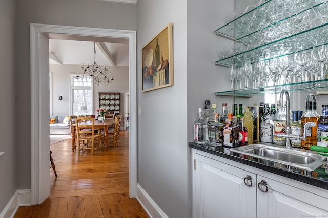 bar with wood-type flooring, sink, a chandelier, and white cabinets