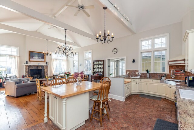 kitchen featuring ceiling fan with notable chandelier, a fireplace, a kitchen bar, and a healthy amount of sunlight