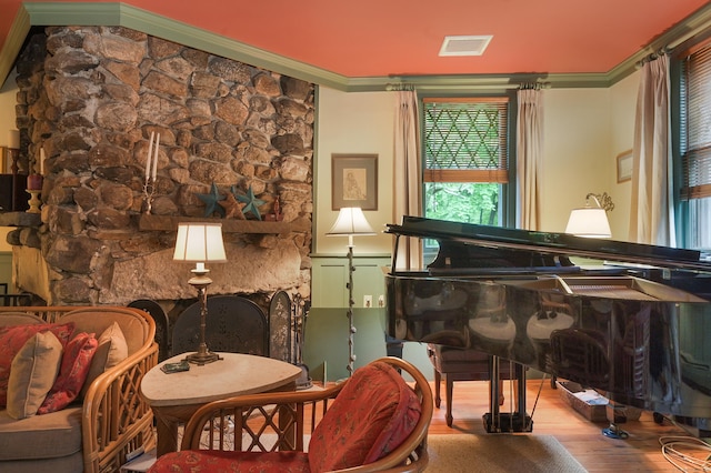 living area featuring a stone fireplace, wood-type flooring, and ornamental molding