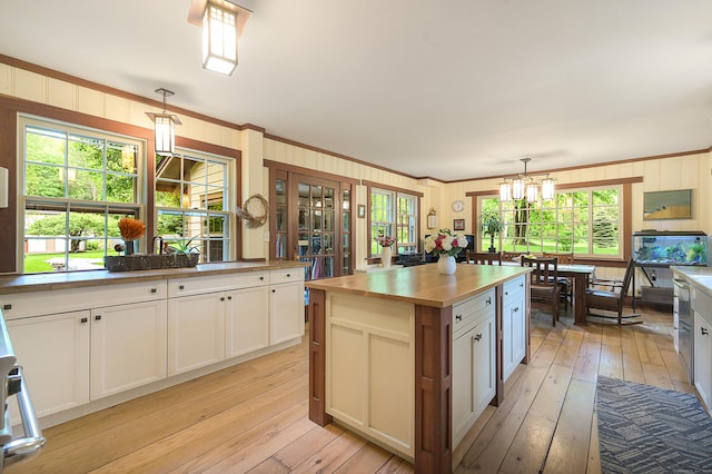 kitchen featuring decorative light fixtures, white cabinetry, a wealth of natural light, and crown molding