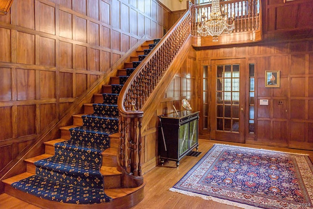 foyer entrance featuring a notable chandelier, a high ceiling, wood walls, and light hardwood / wood-style flooring