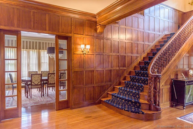 staircase featuring an inviting chandelier, wooden walls, light hardwood / wood-style floors, and ornamental molding