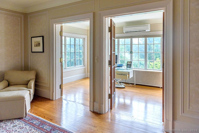 doorway to outside with plenty of natural light, a wall mounted air conditioner, and light hardwood / wood-style flooring