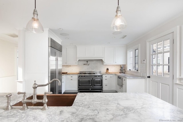kitchen with tasteful backsplash, sink, pendant lighting, built in appliances, and white cabinetry