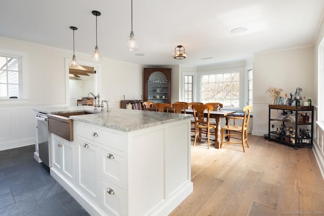 kitchen with a kitchen island with sink, hanging light fixtures, stainless steel dishwasher, light hardwood / wood-style floors, and white cabinetry