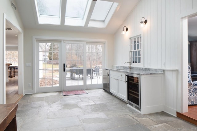 interior space featuring light stone countertops, lofted ceiling with skylight, beverage cooler, sink, and white cabinets