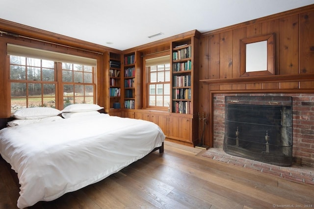 bedroom featuring hardwood / wood-style flooring, a brick fireplace, crown molding, and wood walls