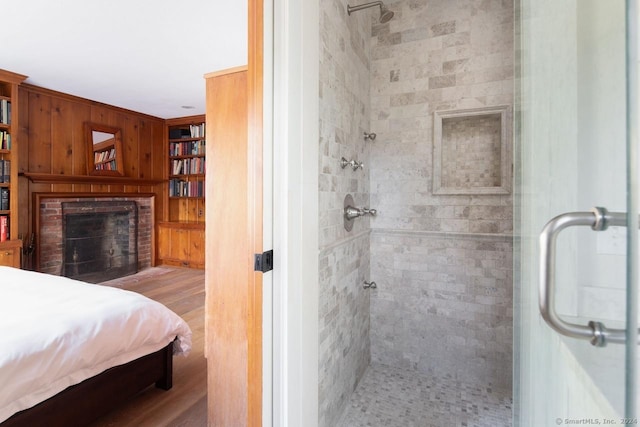 bathroom featuring hardwood / wood-style flooring, wood walls, an enclosed shower, and a brick fireplace
