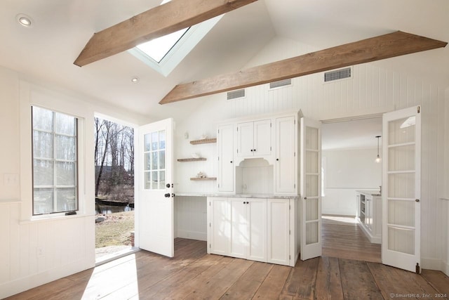 kitchen with vaulted ceiling with skylight, white cabinets, and light hardwood / wood-style flooring