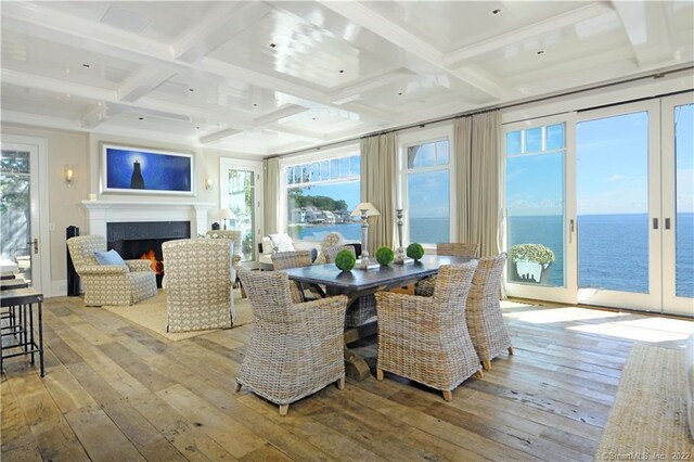 dining room with light hardwood / wood-style floors, a water view, and coffered ceiling