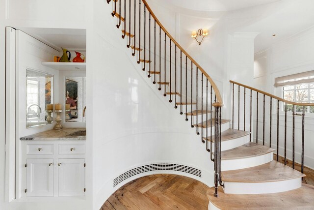 staircase with crown molding and parquet floors