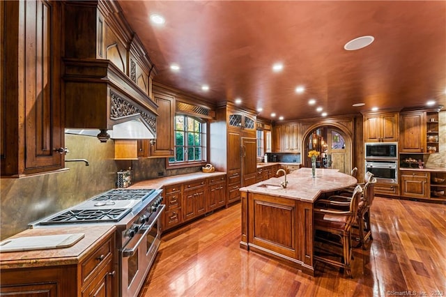 kitchen with backsplash, dark hardwood / wood-style floors, stainless steel appliances, and an island with sink