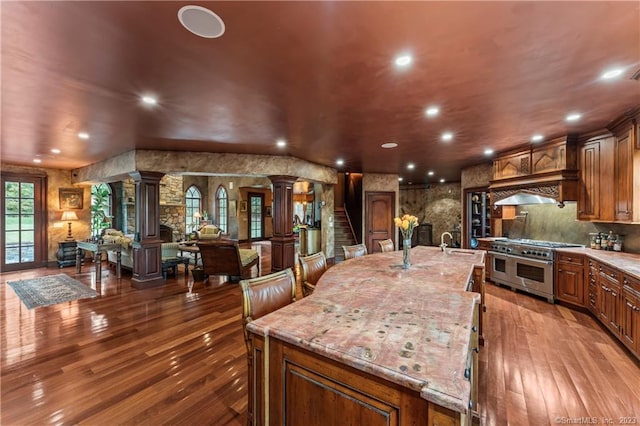 kitchen with a large island with sink, light stone counters, wood-type flooring, and ornate columns