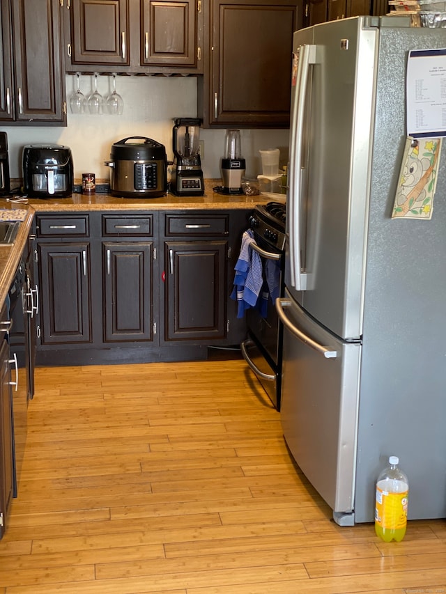 kitchen with stainless steel refrigerator, dark brown cabinets, black range with gas cooktop, and light hardwood / wood-style flooring