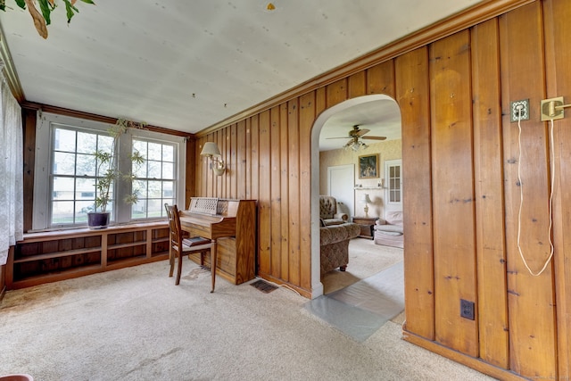 carpeted home office with ornamental molding, wood walls, and ceiling fan