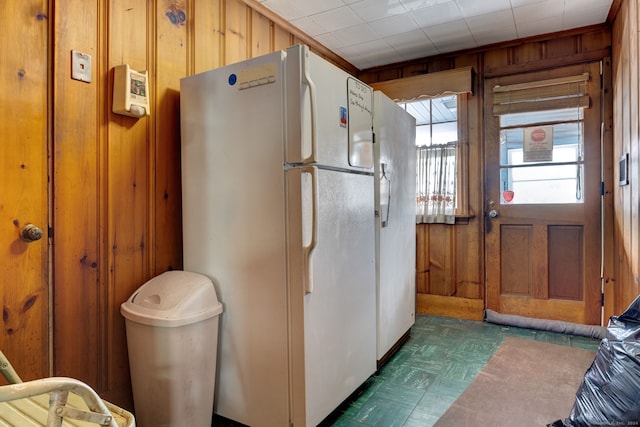 kitchen with wooden walls, dark tile flooring, and white fridge