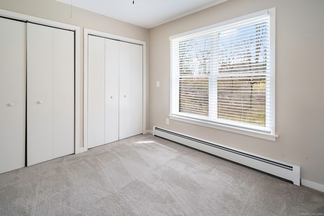 unfurnished bedroom featuring light carpet, two closets, and baseboard heating