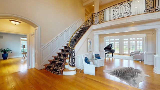 staircase featuring light hardwood / wood-style flooring, a towering ceiling, crown molding, and decorative columns