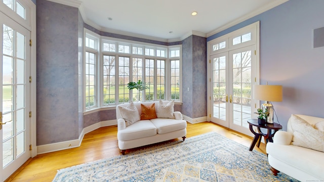 sitting room with french doors, crown molding, and light wood-type flooring