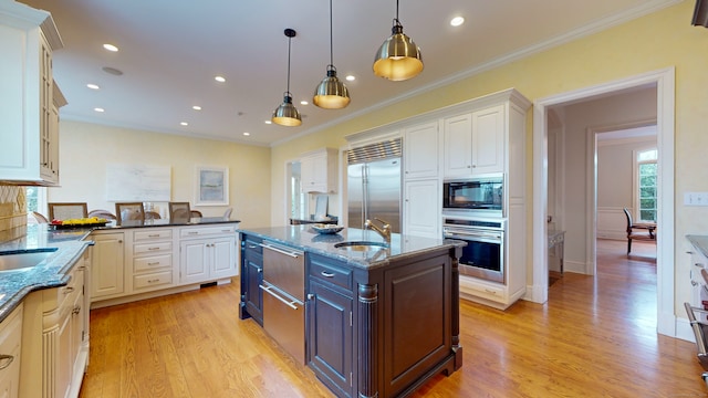 kitchen featuring hanging light fixtures, light wood-type flooring, a kitchen island with sink, and built in appliances