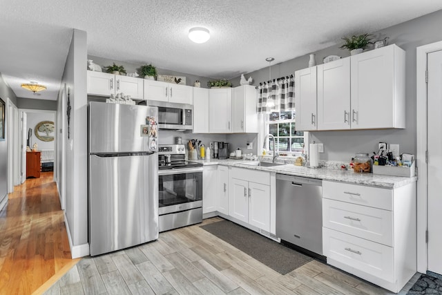 kitchen with appliances with stainless steel finishes, white cabinetry, light hardwood / wood-style flooring, and sink