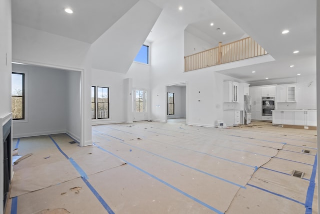 unfurnished living room with recessed lighting, plenty of natural light, a towering ceiling, and baseboards