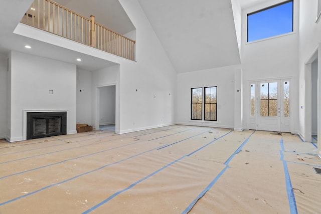 unfurnished living room featuring recessed lighting, a fireplace, a towering ceiling, and baseboards