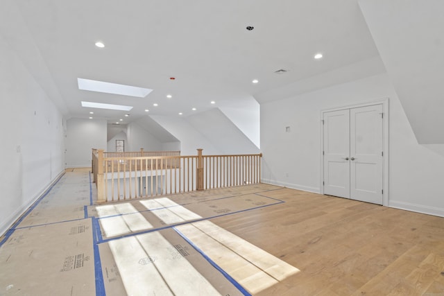 additional living space featuring vaulted ceiling with skylight and light wood-type flooring