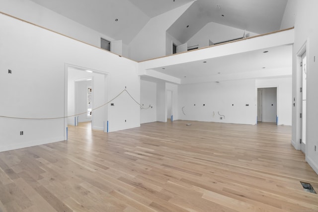 unfurnished living room with light wood-type flooring and a towering ceiling