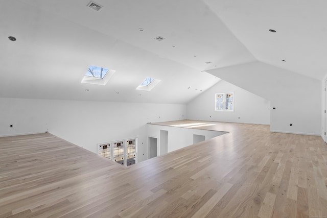 bonus room with lofted ceiling with skylight and light wood-type flooring