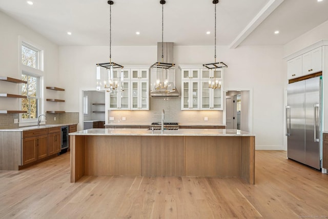 kitchen featuring tasteful backsplash, a center island with sink, stainless steel built in fridge, light hardwood / wood-style floors, and white cabinetry